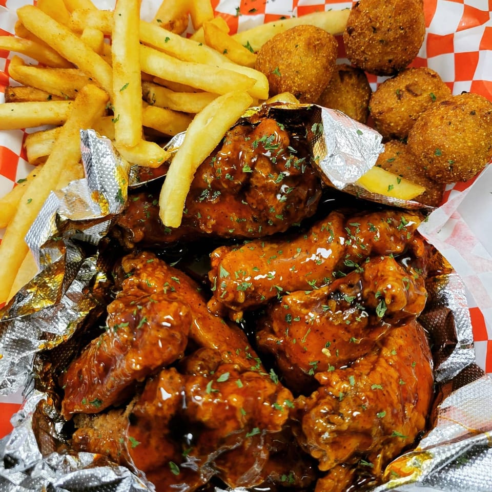 Louisiana Famous Fried Chicken wings with fries and hushpuppies in a red and white checkered basket.