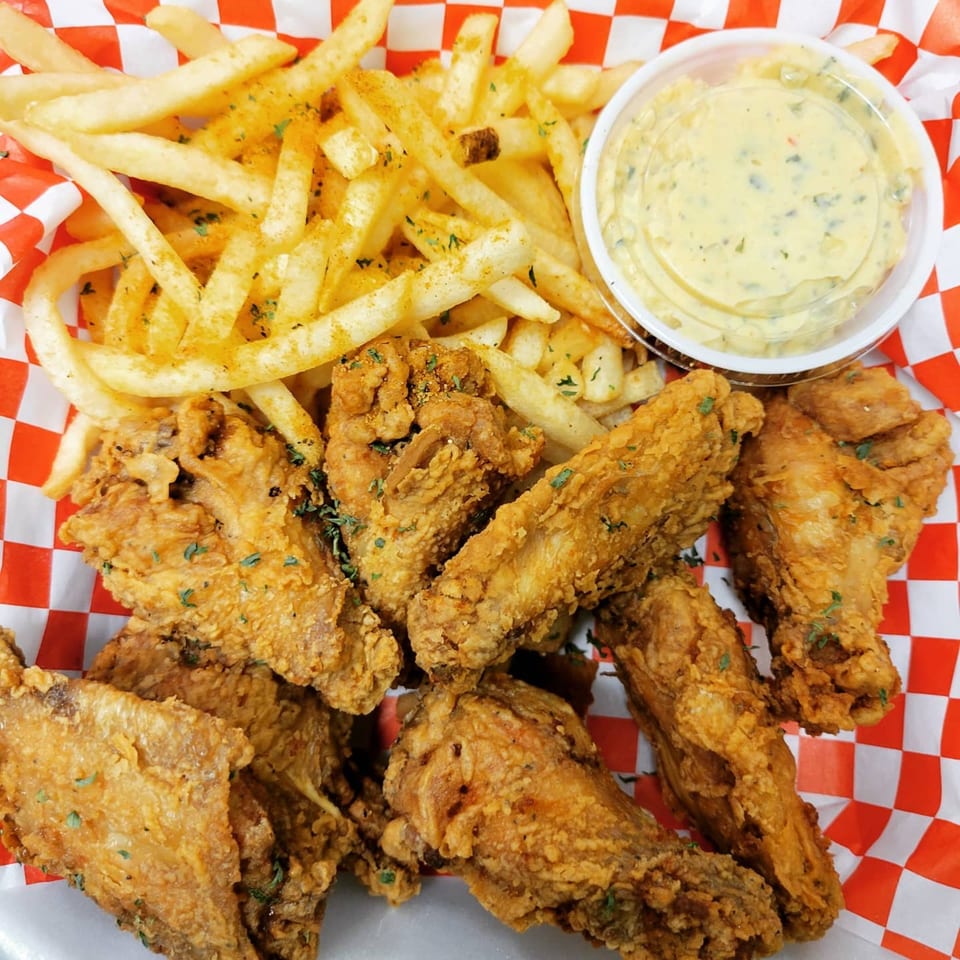 Louisiana Famous Fried Chicken wings and fries with dipping sauce in a red and white checkered basket.