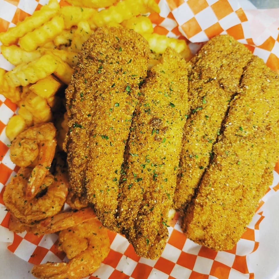 Louisiana Famous Fried Chicken's fried fish fillets, shrimp, and crinkle-cut fries on a checkered paper.